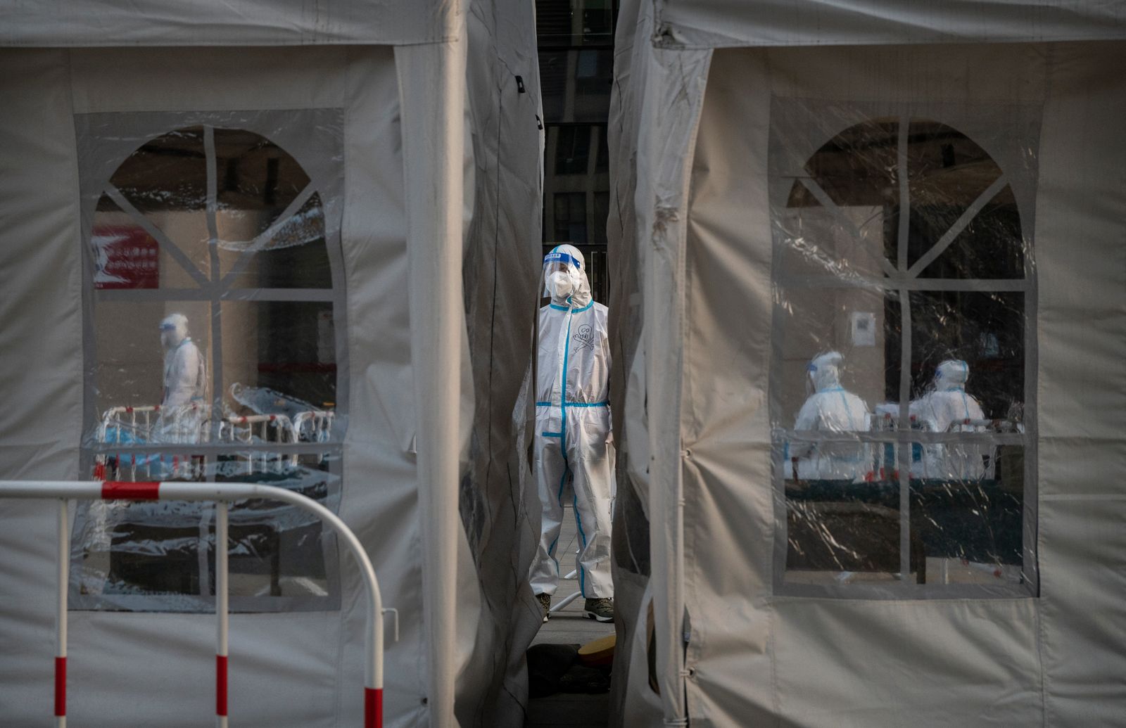 A health worker dressed in protective clothing stands between two white COVID-19 testing tents