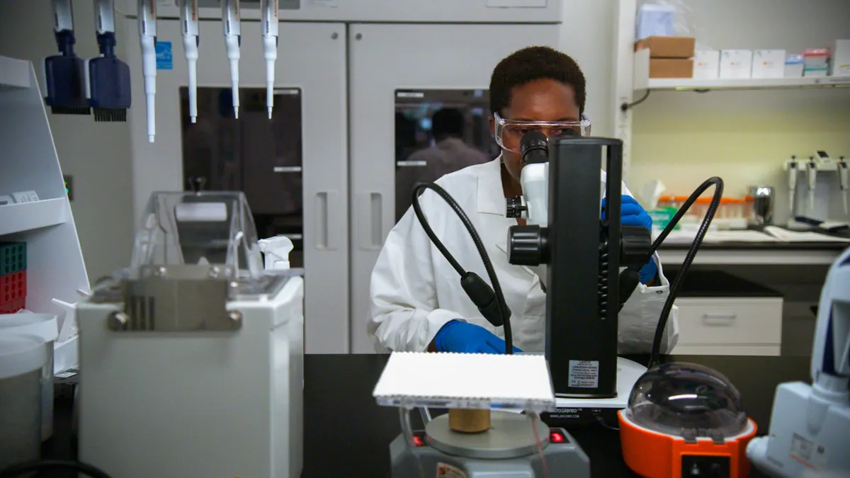 A person wearing a white coat works at a research laboratory bench.