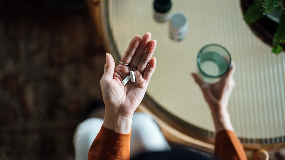 Overhead view of a person holding two white pills in their left hand and a glass of water in their right hand.