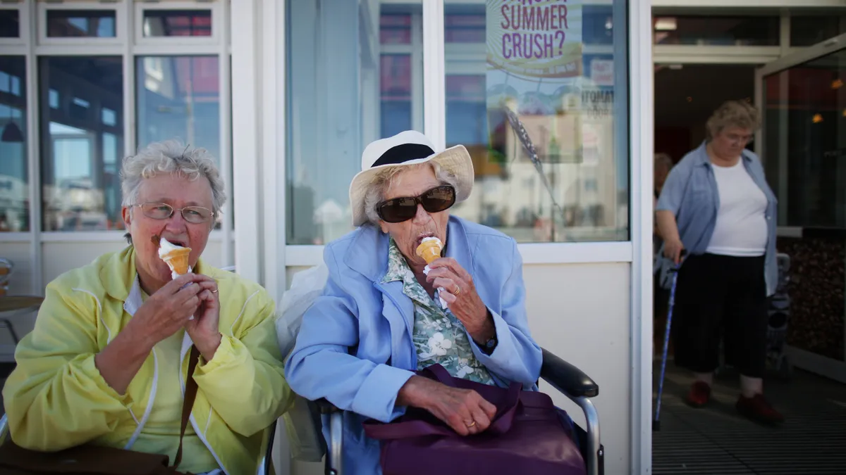 Two grey haired women sit on a bench eating ice cream