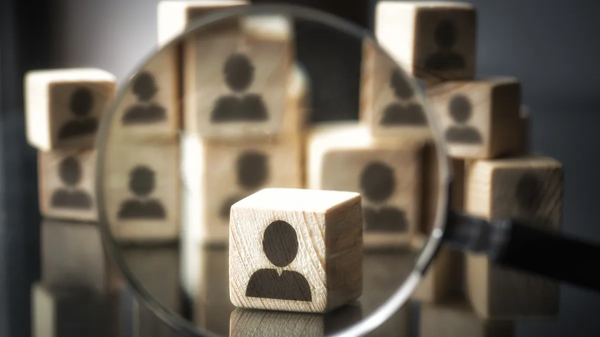 A magnifying glass is held over a wooden block with a business person's silhouette etched on it.