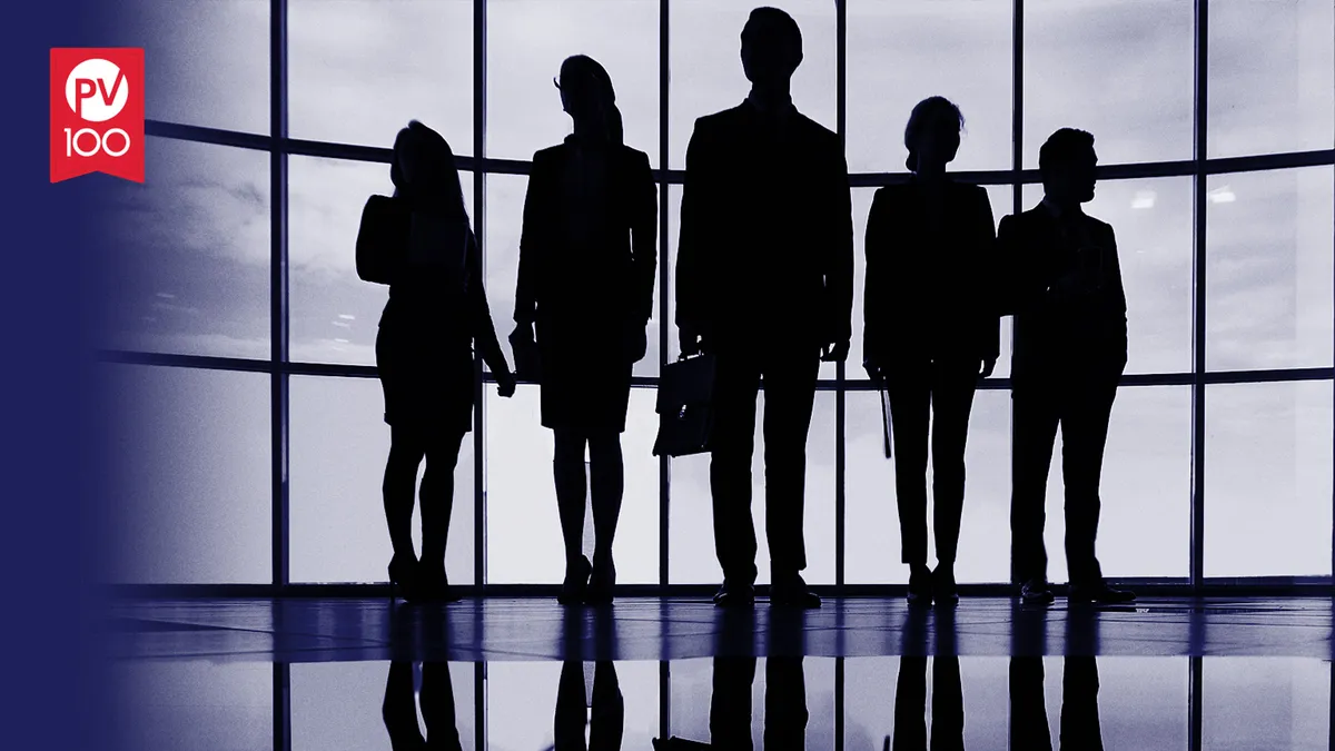 Silhouette of people in business attire in front of a wall of windows