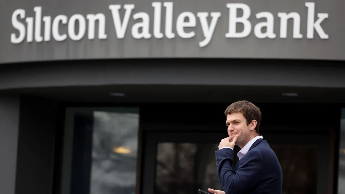 A person stands outside of a building that says 'Silicon Valley Bank' with their hand on their chin.